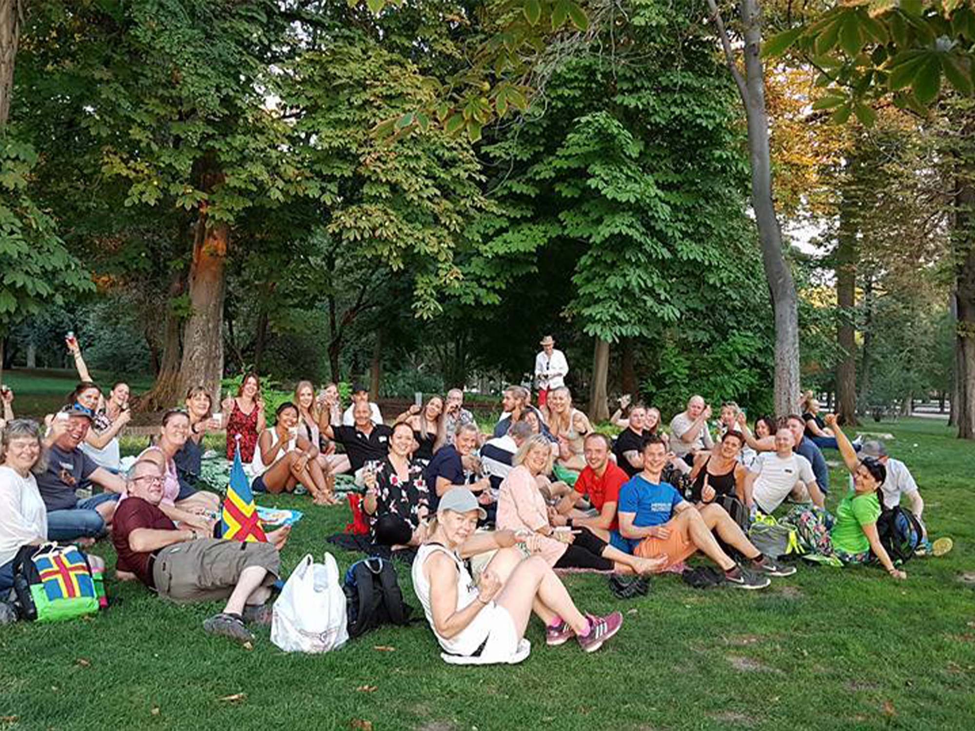 Extravaganza-Madrid En stor grupp med människor sitter på gräset och ser glatt in i kameran.