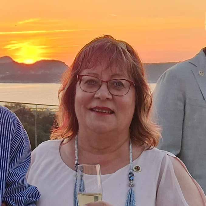 Monica Porträttbild på Monica. Hon har axellångt hår, röda glasögon och håller ett glas bubbel i handen. I bakgrunden syns en solnedgång.