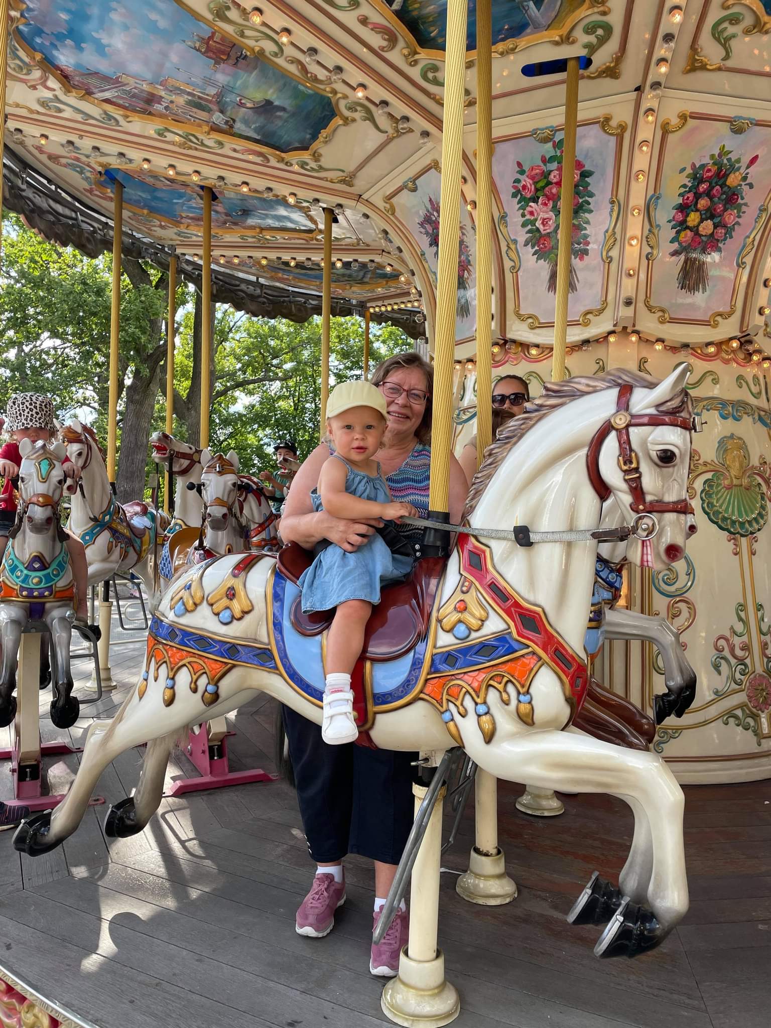 Tid med barnbarn En leende kvinna håller i ett barn som rider på en karusellhäst.